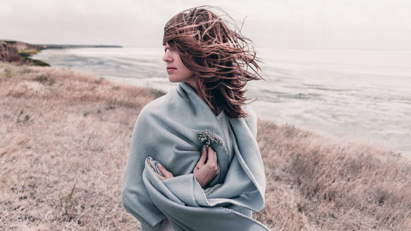 Attractive,Young,Woman,Standing,On,A,Windy,Cold,Beach,Wrapped