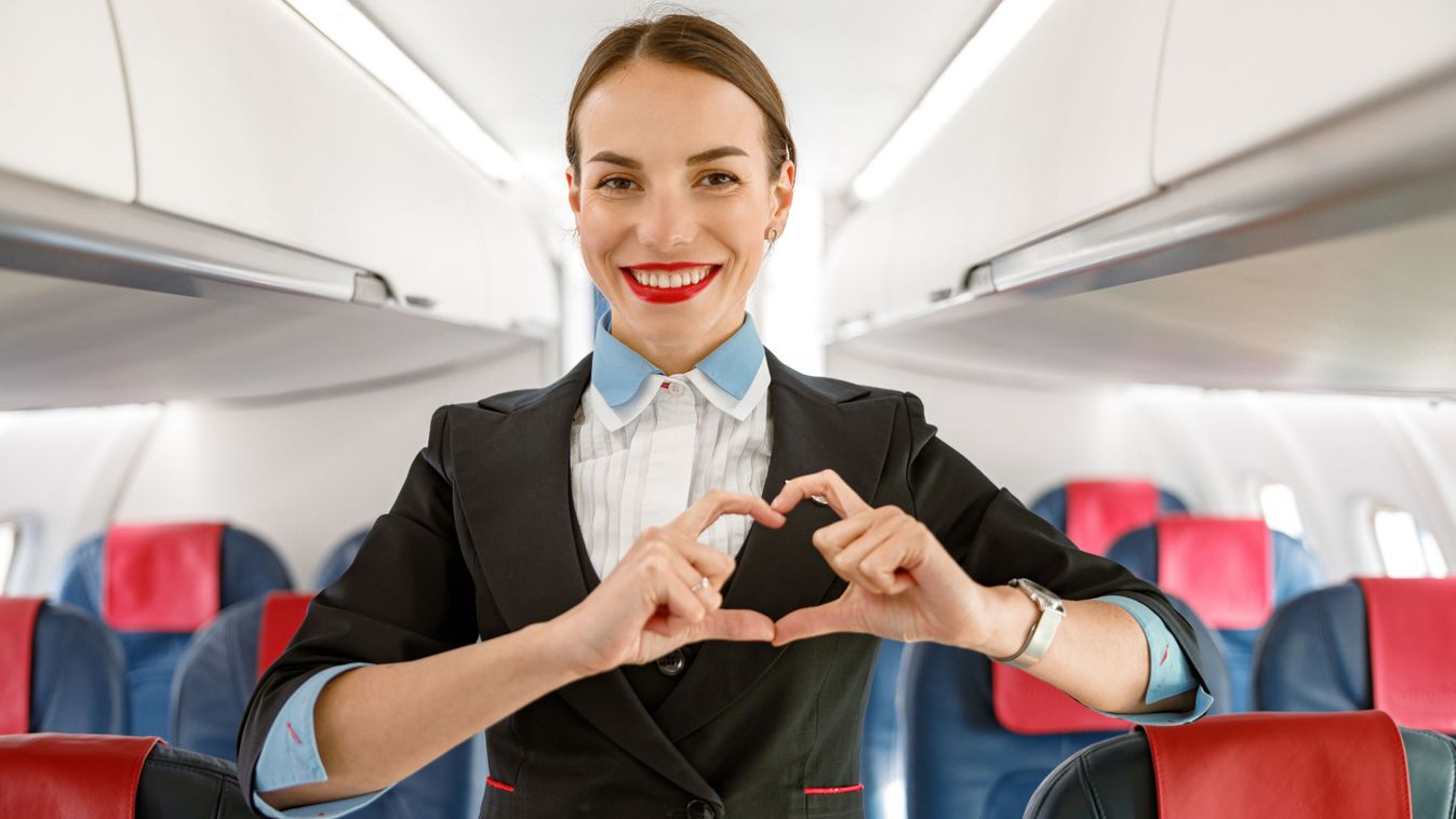 Cheerful,Woman,Stewardess,Doing,Heart,Sign,In,Airplane