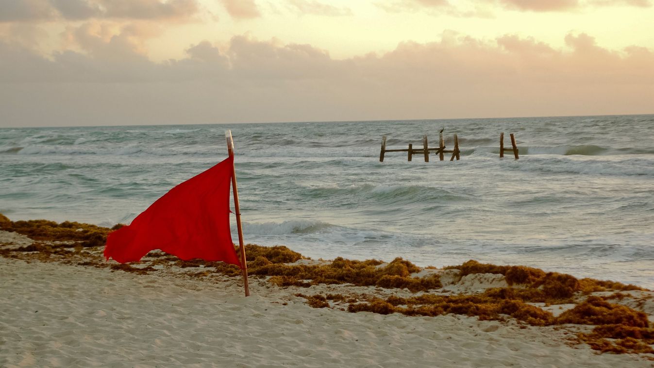 Red,Flag,Waving,On,The,Beach,At,Sunrise,With,Rough