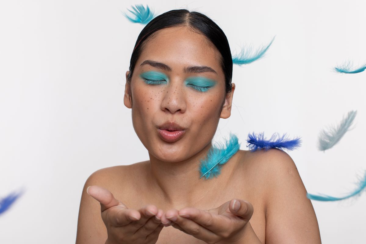 Woman,Wearing,Blue,Makeup,Blowing,On,Blue,Feathers