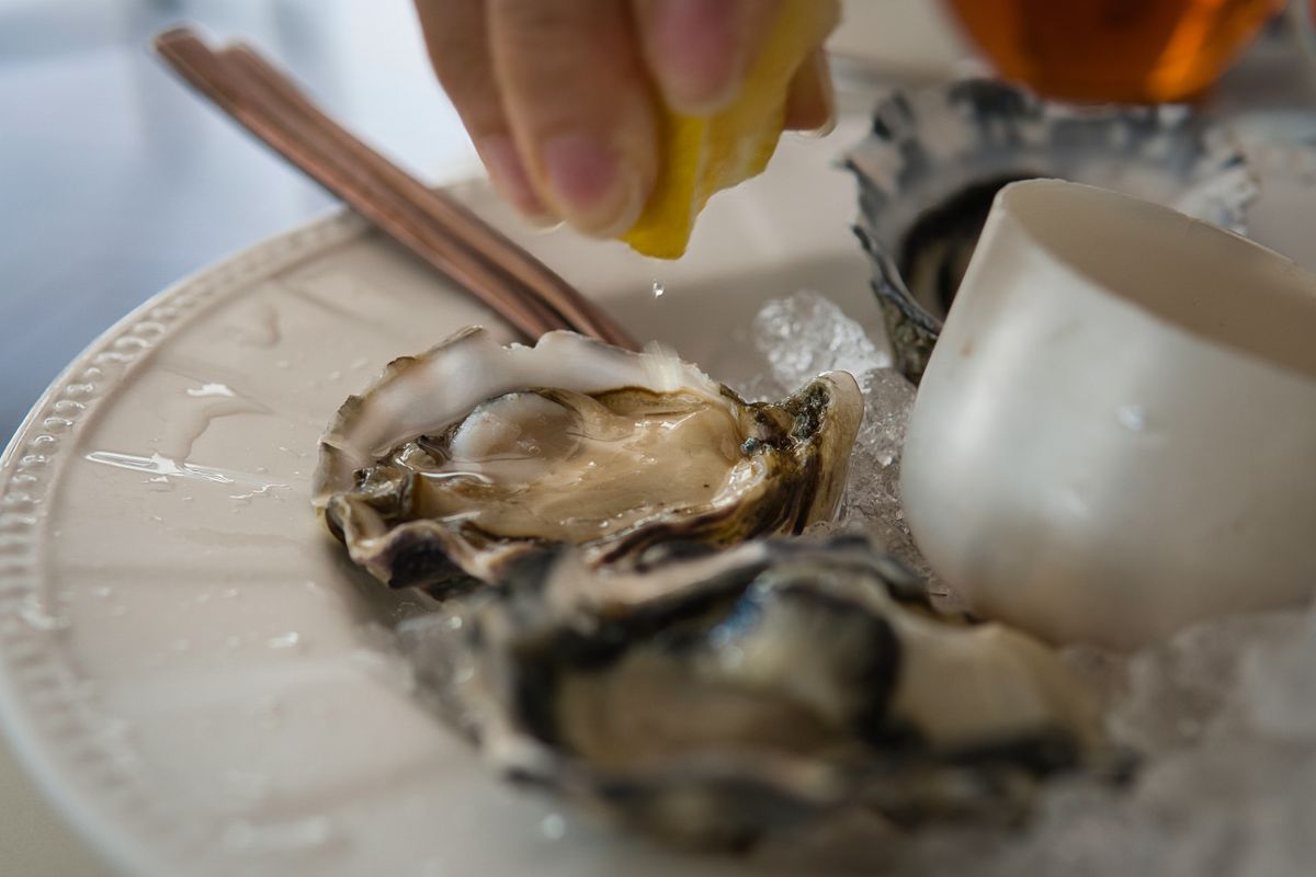 Hand,Squeezing,Lemon,Juice,Onto,Fresh,Oysters,On,White,Plate
osztriga