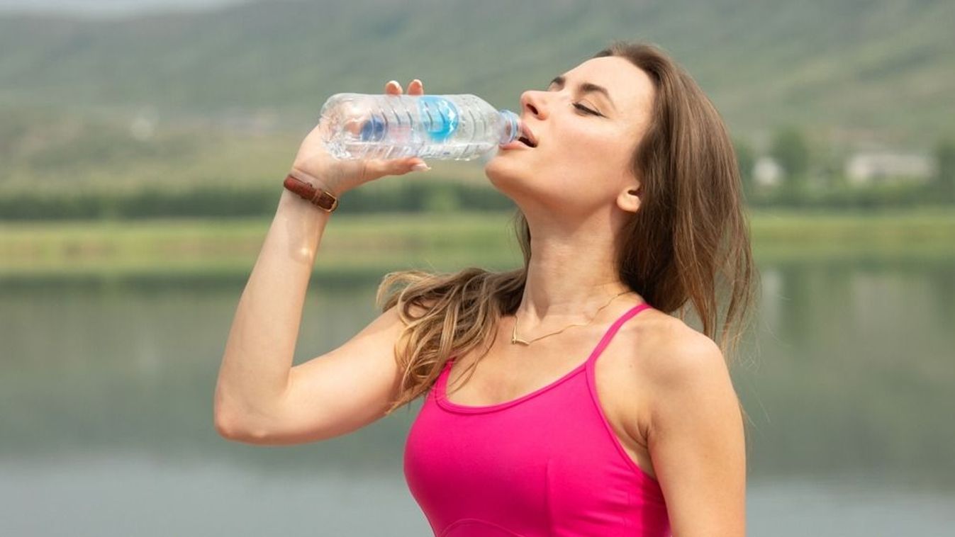 A,Woman,Is,Drinking,Water,While,Standing,By,A,Lake.