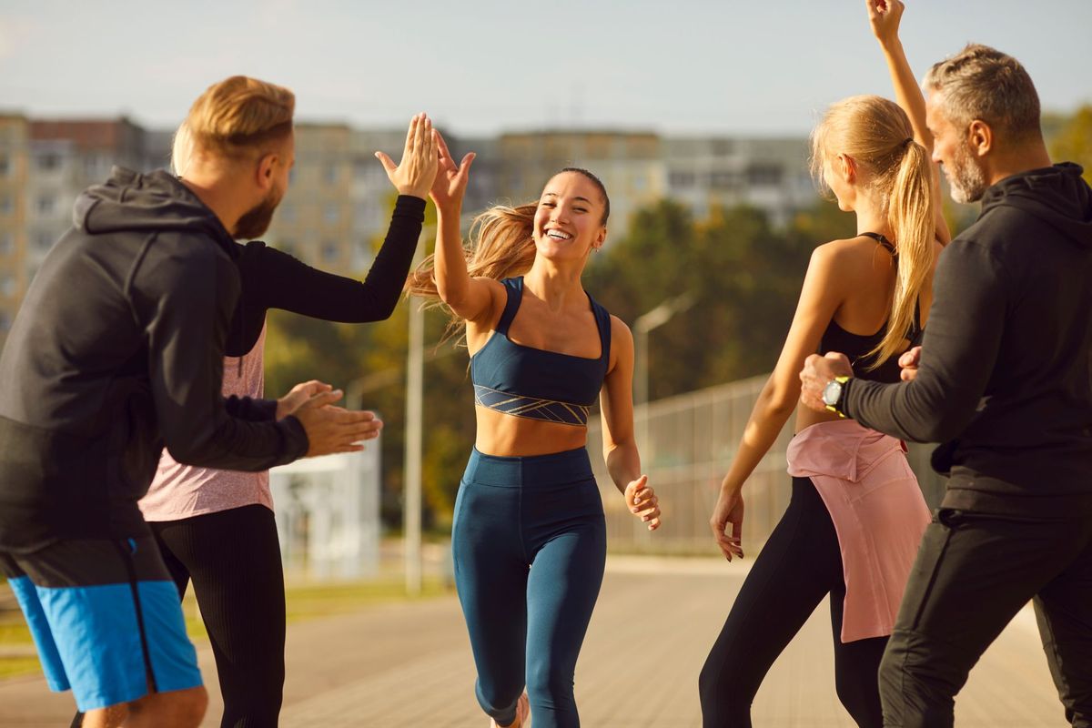 Happy young people giving high five to a woman rejoicing the success in sport training outdoors.