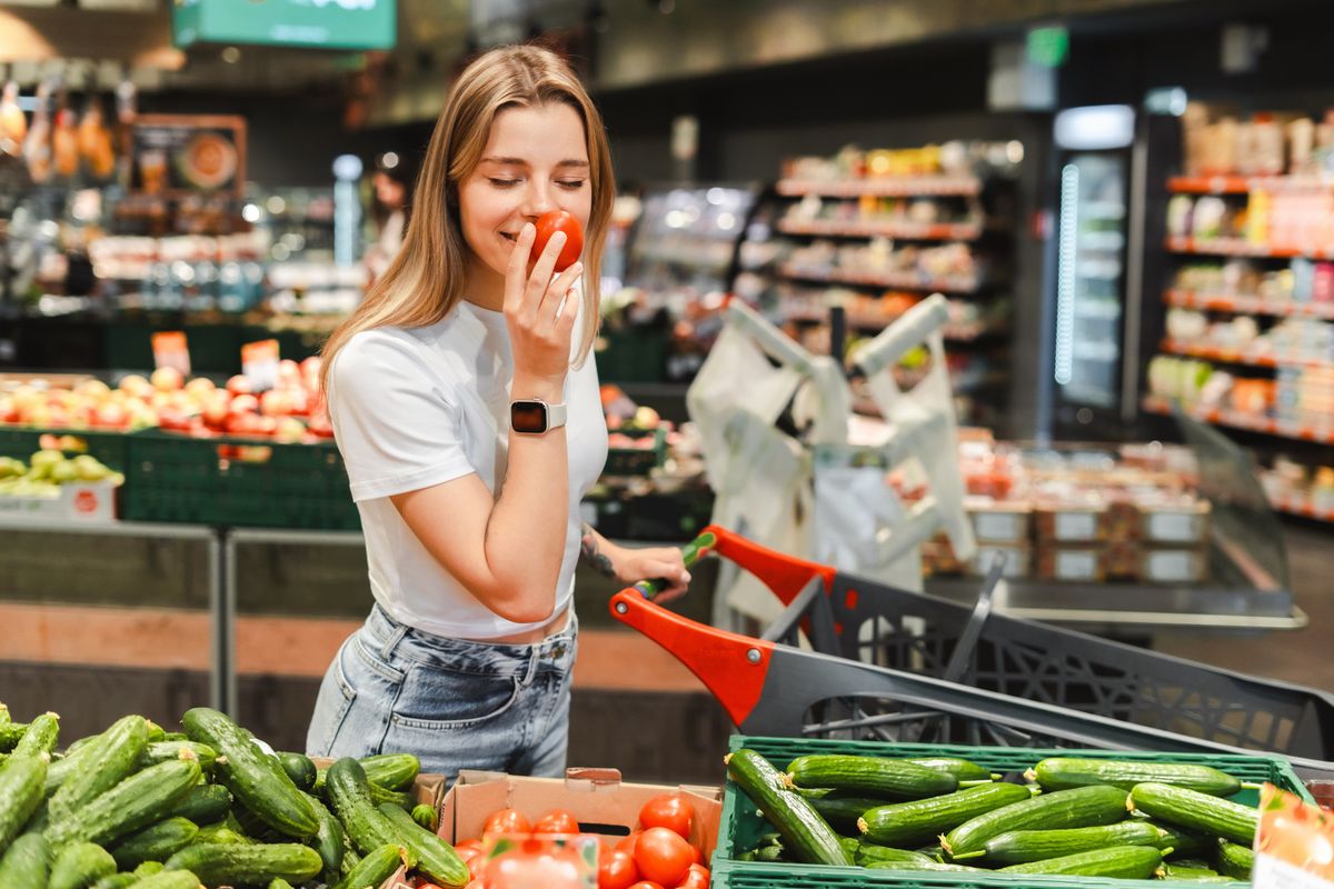 Young,Woman,Smelling,A,Tomato,While,Grocery,Shopping,In,A