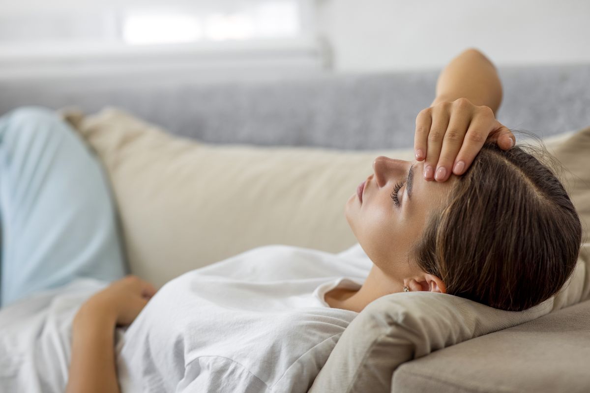 Woman laying on sofa eyes closed feeling unwell