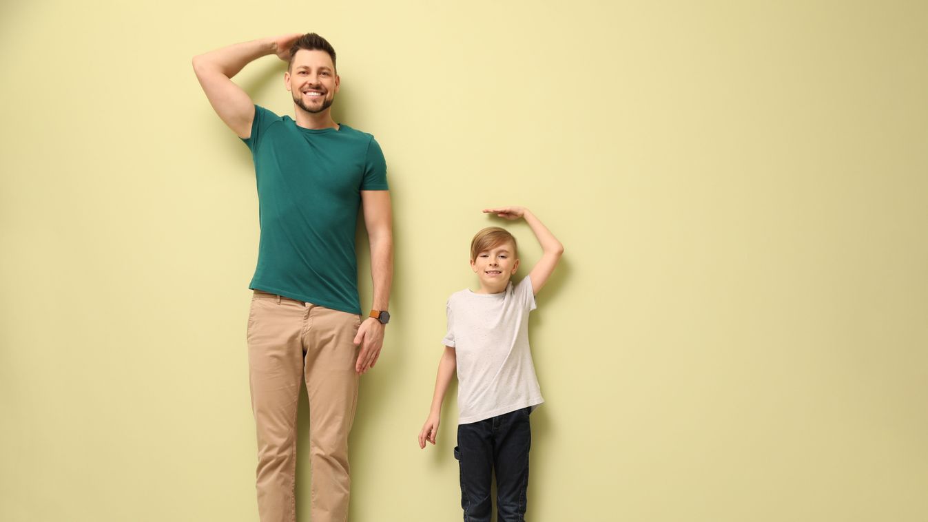 Father,And,Son,Comparing,Their,Heights,Near,Light,Wall,Indoors.