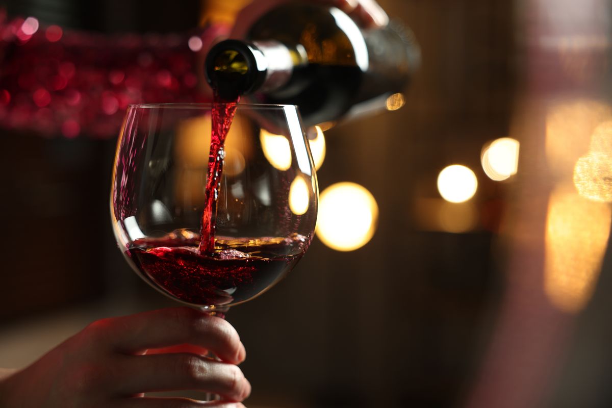 Woman,Pouring,Red,Wine,From,Bottle,Into,Glass,On,Blurred