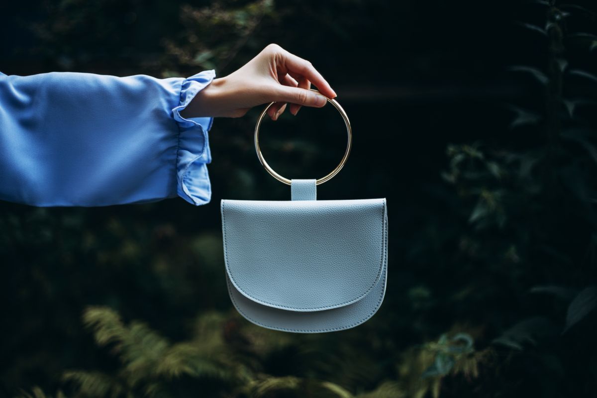 A woman's hand holds handbag in her hand on a dark background