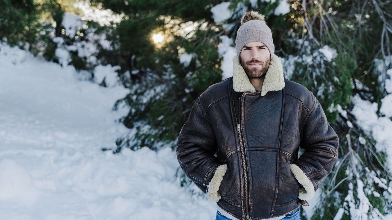 Young man with hands in pockets of standing against trees in snow