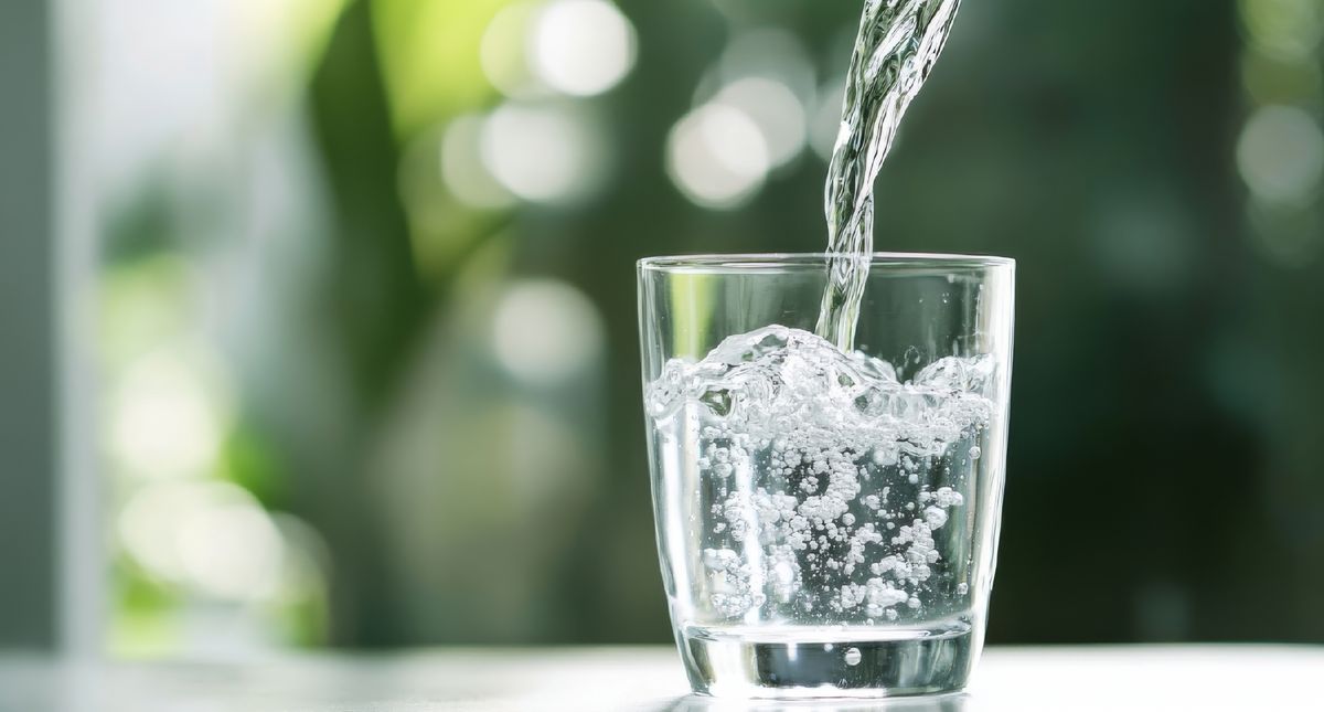 Pouring,Water,Into,A,Glass,Against,A,Green,Blurred,Background