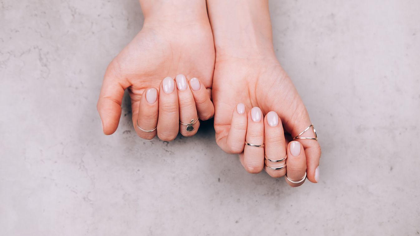 Woman hands with nude pink manicure and with many various silver rings on fingers on concrete gray background. Concept of trendy boho style. Flat lay style with copy space