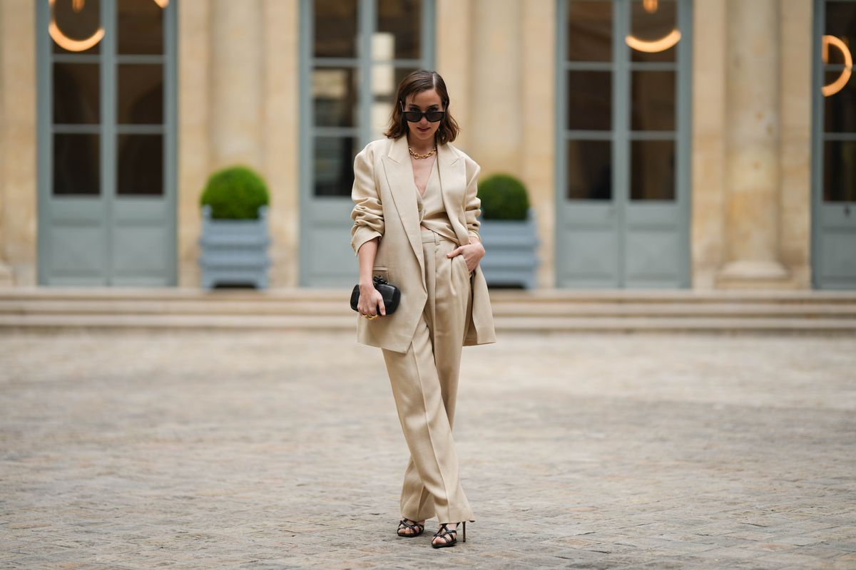 PARIS, FRANCE - APRIL 26: Beatrice Granno wears black sunglasses, a gold large chain necklace, a beige linen V-neck / buttoned suit gilet, a matching beige linen blazer jacket, matching beige linen large suit pants, a black shiny leather clutch, gold rings, black shiny leather strappy heels sandals , outside the COS show, on April 26, 2023 in Paris, France. (Photo by Edward Berthelot/Getty Images )