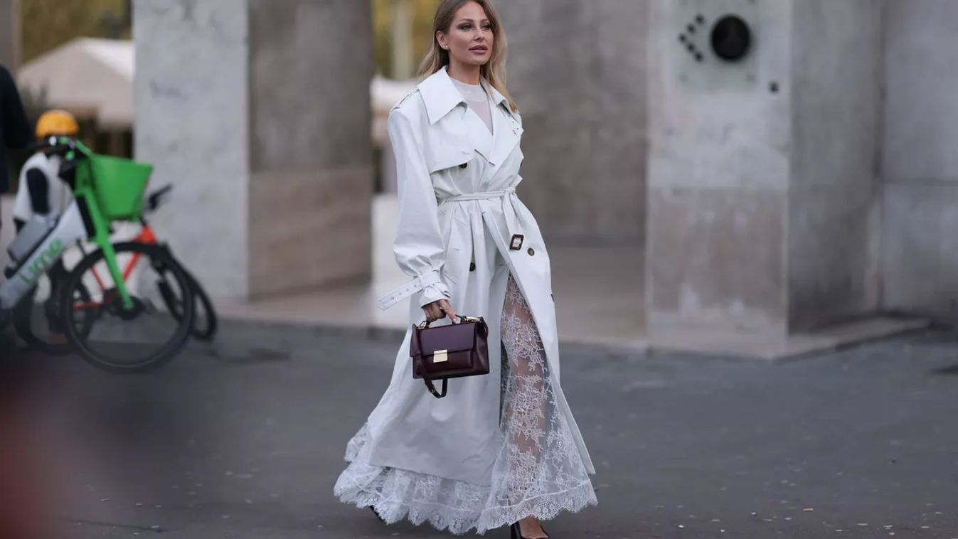 PARIS, FRANCE - SEPTEMBER 29: Ginta is seen wearing two round diamond stud earrings; an outfit from Vassia Kostara, consisting of a calf-length white leather trench coat featuring a brown double-button placket, a belt, and oversized lapels, layered over a