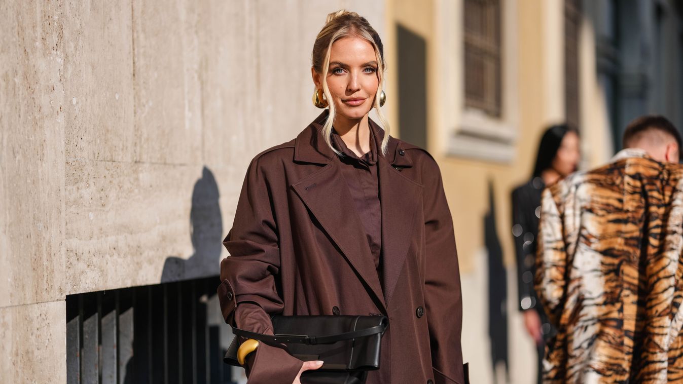 MILAN, ITALY - FEBRUARY 27: Leonie Hanne wears dark brown sunglasses, gold earrings, dark brown cropped long sleeve Max Mara shirt, dark brown Max Mara trench coat, shiny black leather bag, gold bangle bracelet, gold bracelet, outside Max Mara, during the