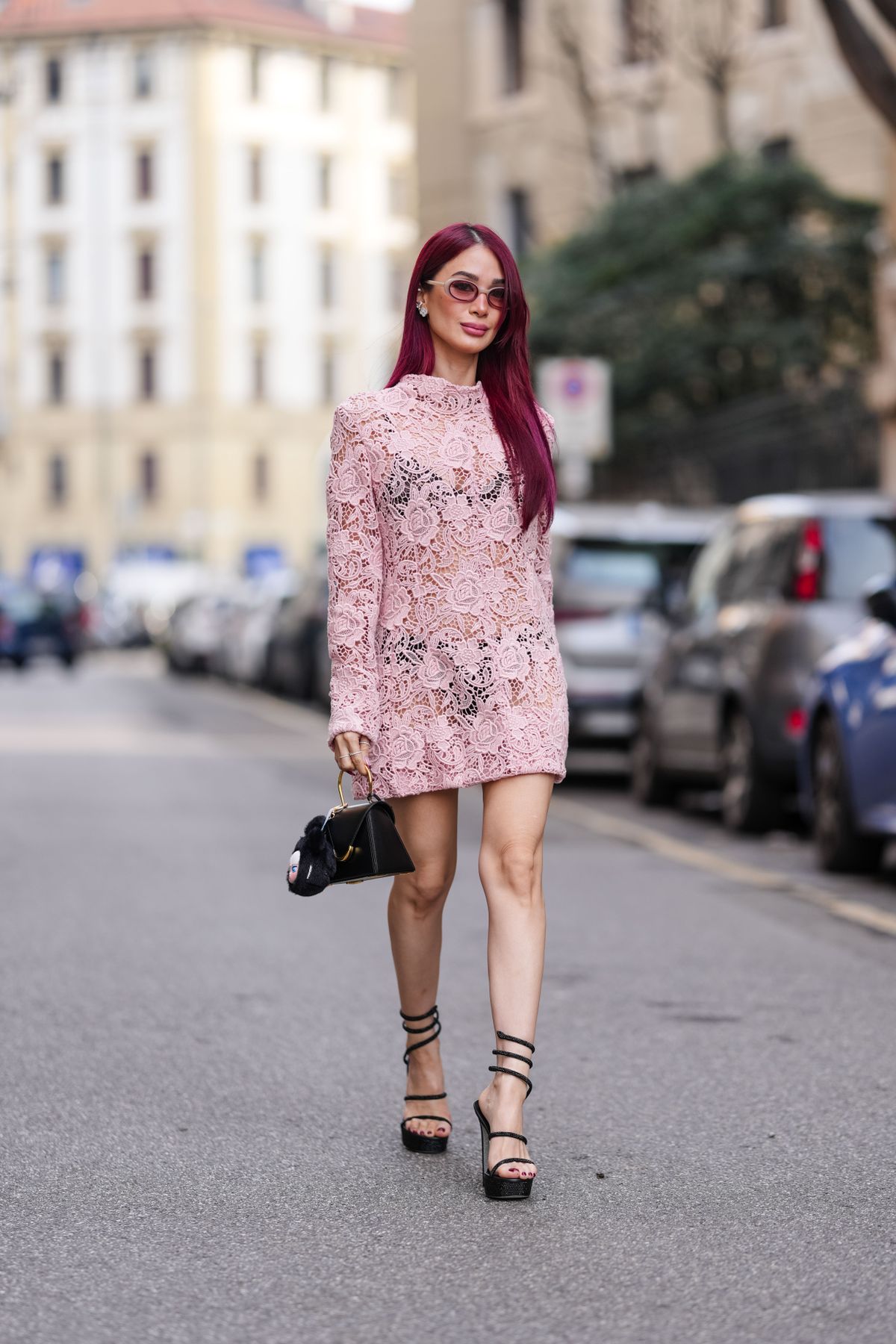 MILAN, ITALY - FEBRUARY 28: Heart Evangelista wears burgundy bordeaux hair, light brown sunglasses, silver earrings, dark pink floral lace sheer mesh long sleeve midi dress, shiny black leather bag, black open toe heels leather shoes, outside Sportmax, during the Milan Fashion week Women's Fall/Winter 2025-2026 on February 28, 2025 in Milan, Italy. (Photo by Edward Berthelot/Getty Images)