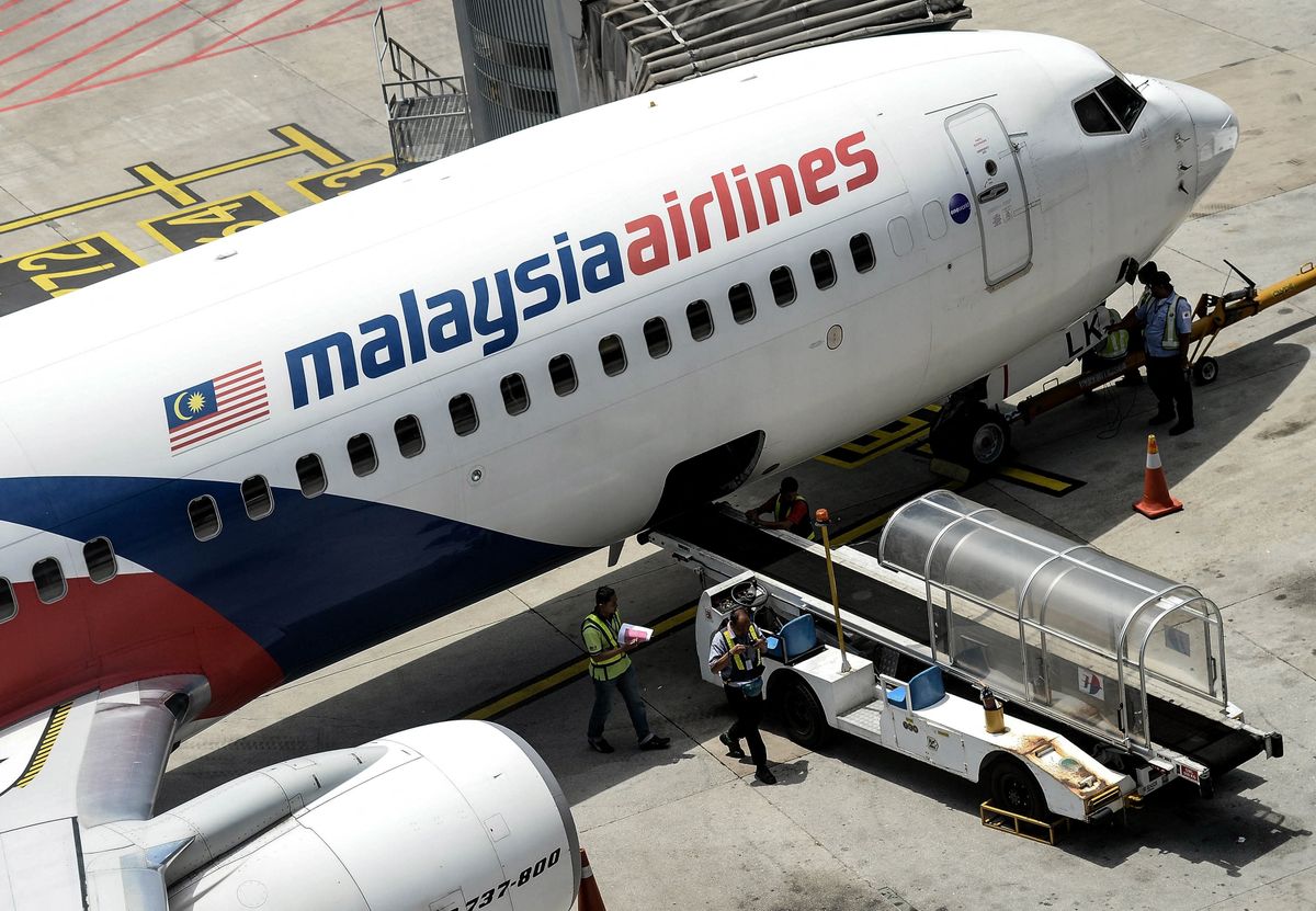 eltűnt maláj gép, Malaysia Airlines ground staff walk on the tarmac next to a Malaysia Airlines plane at Kuala Lumpur International Airport in Sepang on February 25, 2016. A fresh search for Malaysia Airlines flight MH370 has been launched more than a decade after the plane went missing in one of aviation's greatest enduring mysteries, with maritime exploration firm Ocean Infinity resuming the hunt for the missing plane, according to Malaysian transport minister Anthony Loke on February 25, 2025. (Photo by Manan VATSYAYANA / AFP)