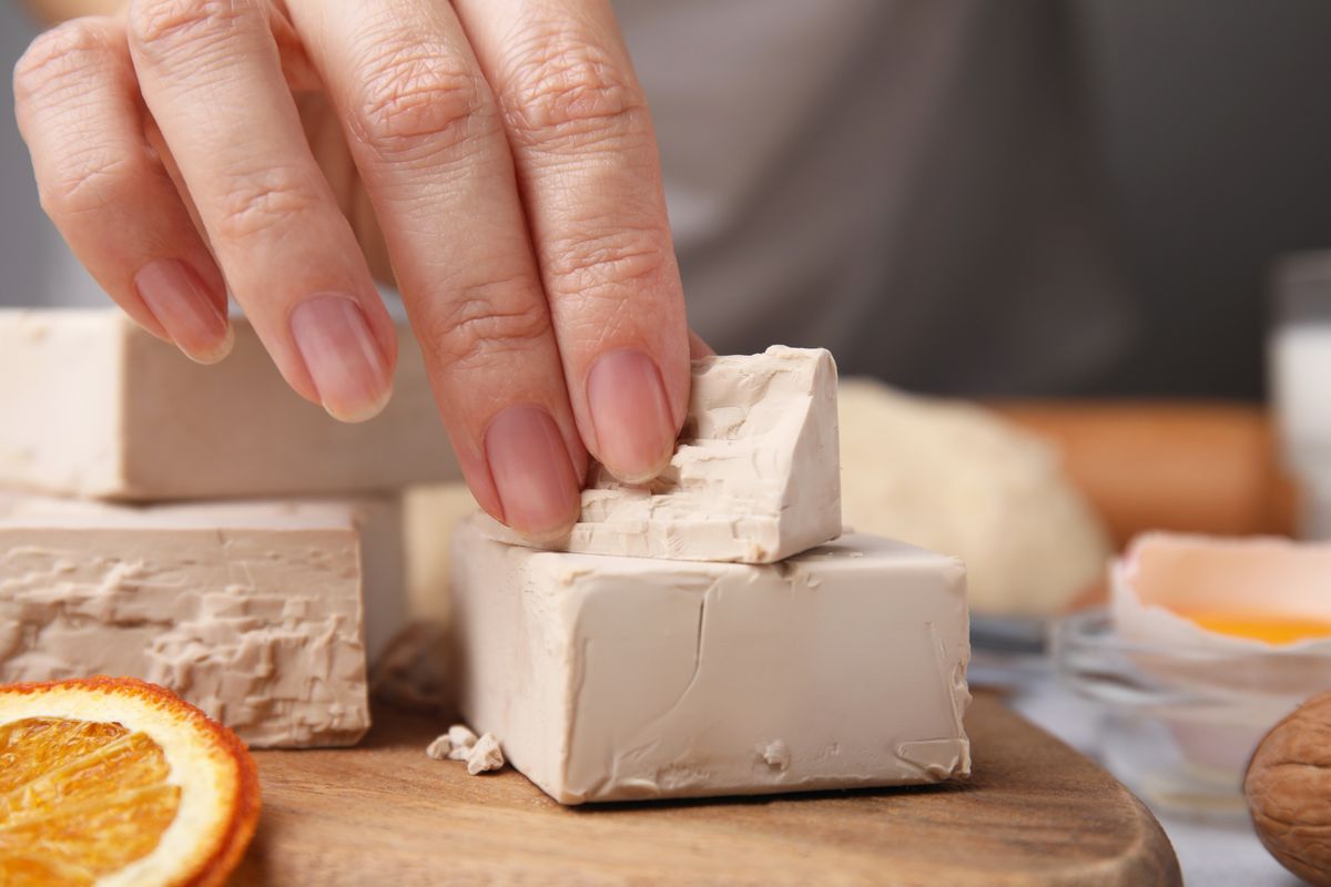 Woman taking piece of compressed yeast at table, closeup, élesztő