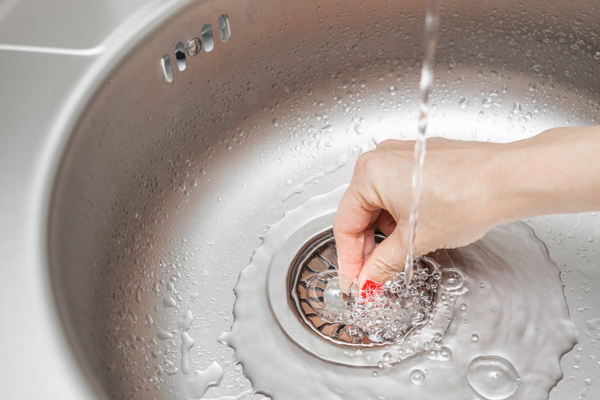 housewife closes the drain hole in the sink. sink drain plug. housewife fills the sink with water. stainless steel sink