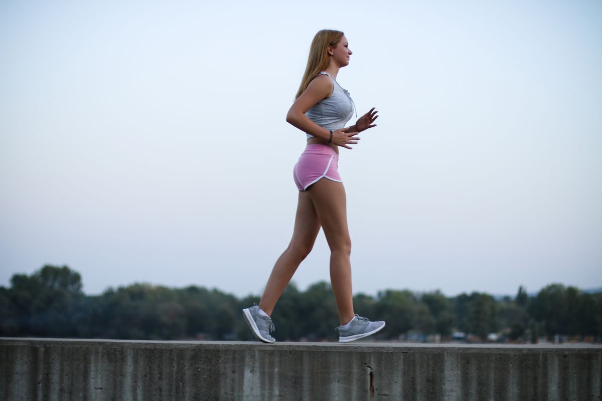 Young sportswoman brisk walking outdoors, urban style.