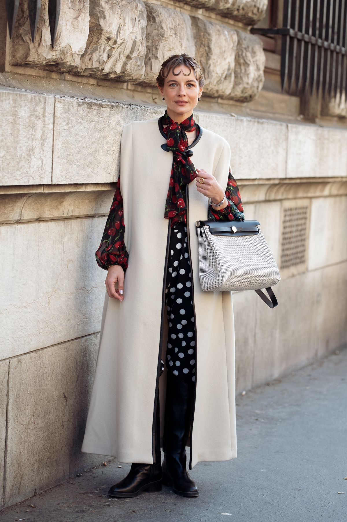 PARIS, FRANCE - MARCH 08: Mafalda Patricio wears black blouse with red cherry print, black and white polka dot pants, black boots, beige cape coat with black leather details, grey Hermes bag, outside the Hermes fashion show during the Womenswear Fall/Winter 2025/2026 as part of Paris Fashion Week on March 08, 2025 in Paris, France. (Photo by Raimonda Kulikauskiene/Getty Images)