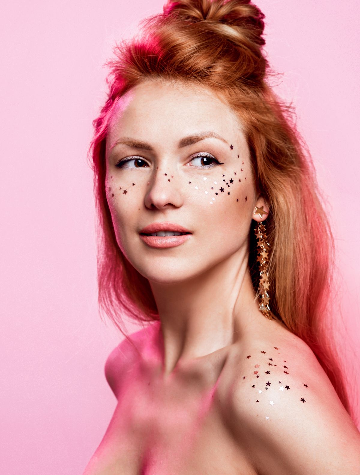 High Fashion model portrait beautiful lips and face woman in colorful pink neon uv lights posing in studio. Beautiful girl with little silver stars confetti colorful make up. Glitter Vivid neon makeup