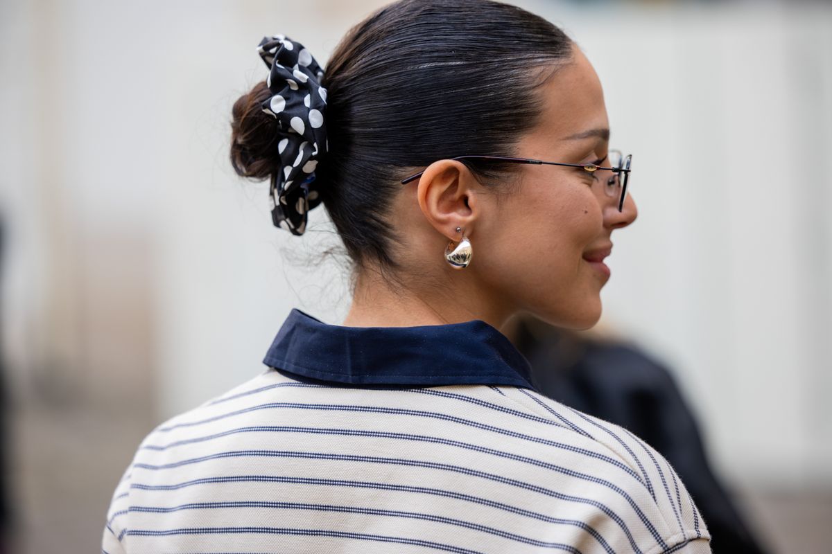 PARIS, FRANCE - MARCH 04: A guest wears striped polo shirt with long sleeves, hair pice with dots print, glasses outside Ganni during the Womenswear Fall/Winter 2025/2026 as part of Paris Fashion Week on March 04, 2025 in Paris, France. (Photo by Christian Vierig/Getty Images)