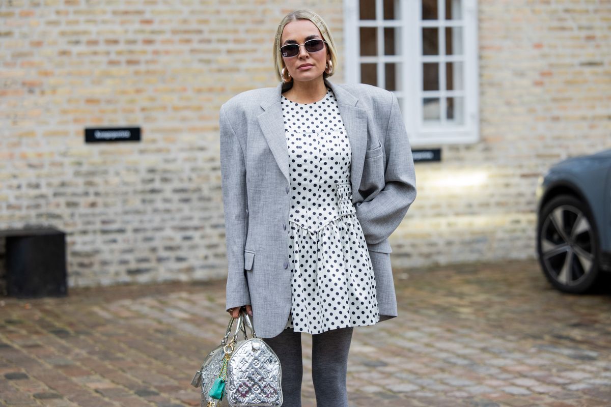 COPENHAGEN, DENMARK - JANUARY 30: A guest wears silver Louis Vuitton bag, grey tights, gauntlets, black heels, white dress with dots print, grey oversized blazer outside Munthe during the Copenhagen Fashion Week Autumn/Winter 2025 on January 30, 2025 in Copenhagen, Denmark. (Photo by Christian Vierig/Getty Images)