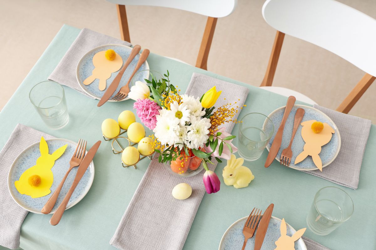 Beautiful table setting for Easter decorated with bouquet of carrots and flowers in dinning room