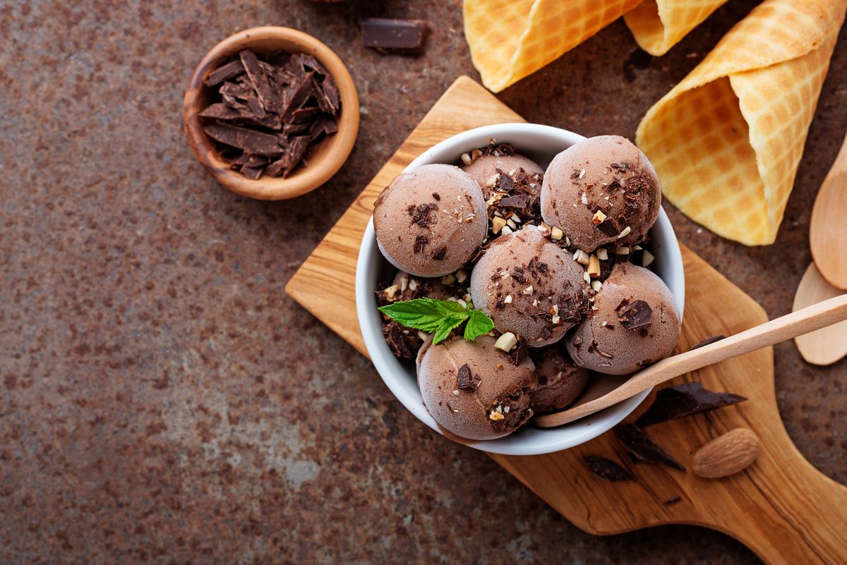 Chocolate ice cream scoops with pieces of chocolate bar and waffle cones on brown background.