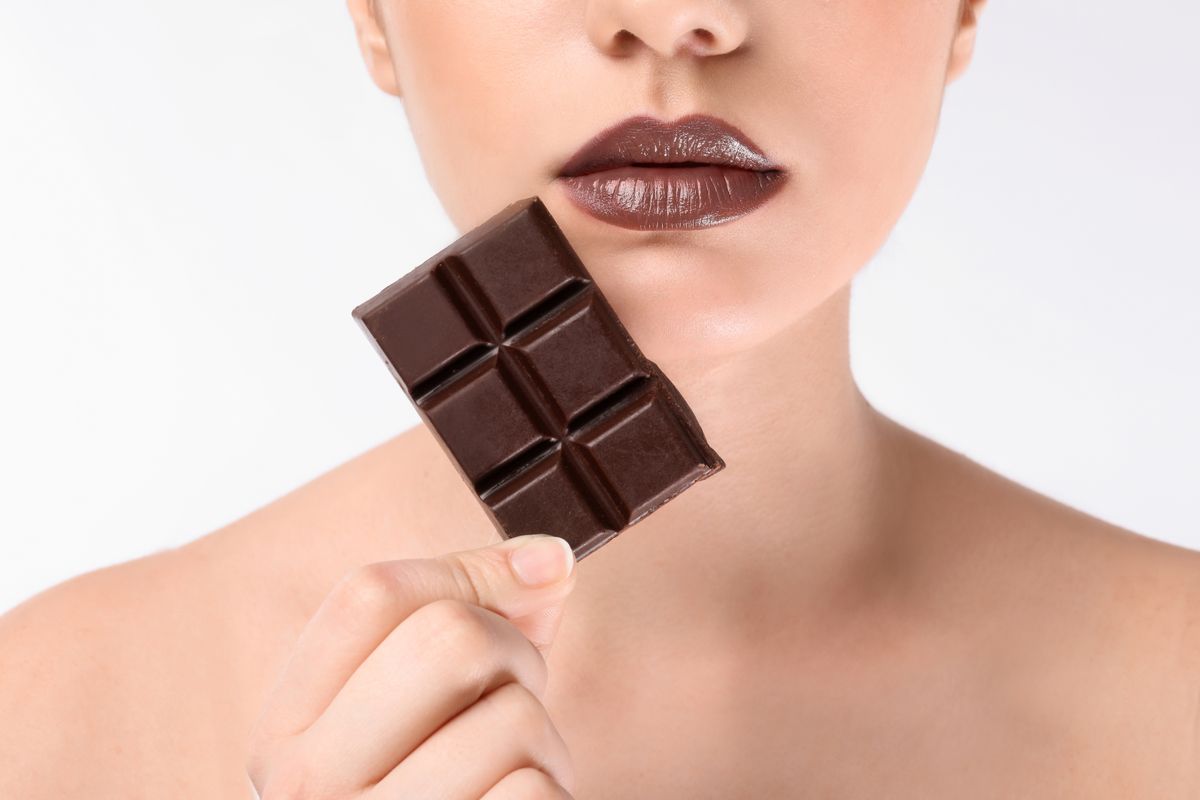 Beautiful young woman with chocolate on white background, closeup