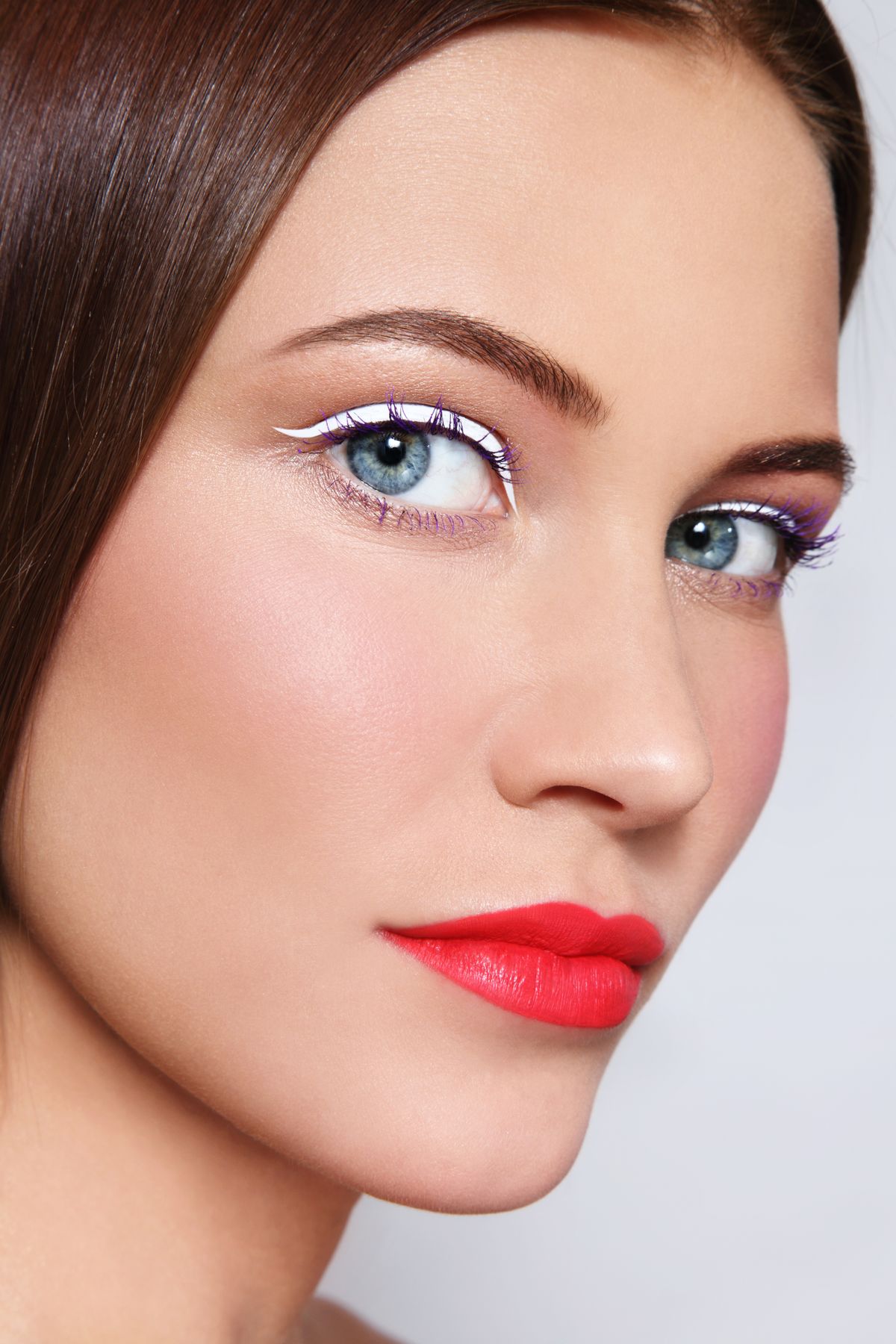 Close-up portrait of young beautiful woman with stylish white eyeliner and coral matte lipstick