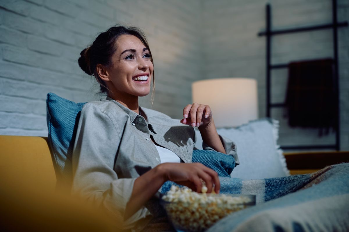Happy woman watching movie and eating popcorn at night at home.