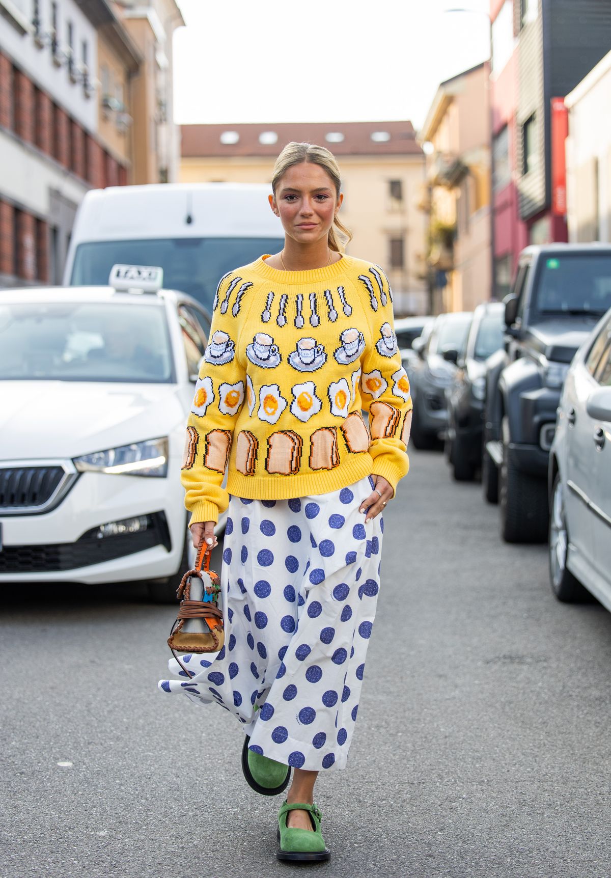 MILAN, ITALY - FEBRUARY 28: Caetana Botelho Afonso wears yellow sweater with graphic print, skirt with dots print, bag outside Moschino during the Milan Fashion Week Womenswear Fall/Winter 2025/2026 on February 28, 2025 in Milan, Italy. (Photo by Christian Vierig/Getty Images)