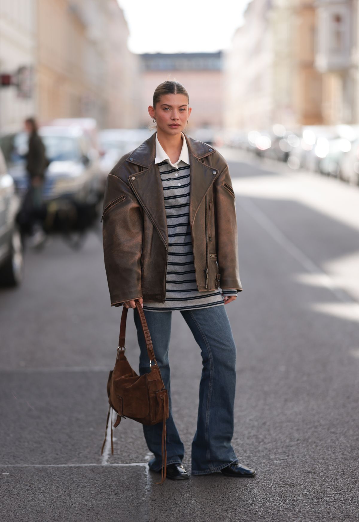 BERLIN, GERMANY - APRIL 08: Sophia Geiss seen wearing minimal hoop earrings, The Frankie Shop grey and navy striped rugby shirt featuring a crisp white polo collar, Ducie London oversized brown leather jacket with a slightly distressed, vintage finish, adding a rugged and effortlessly cool vibe to the outfit, Mango classic bootcut jeans in a medium blue wash, medium-sized brown suede vintage shoulder bag with braided leather straps and long fringe detailing and Jil Sander black, pointed leather boots, on April 08, 2025 in Berlin, Germany. (Photo by Jeremy Moeller/Getty Images)