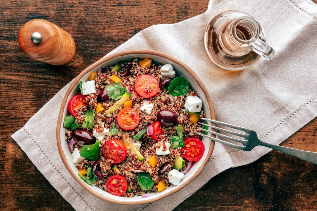 Quinoa salad, healthy Mediterranean lunch with fresh organic vegetables, cheese, and olives, overhead flat lay shot on a wooden background
