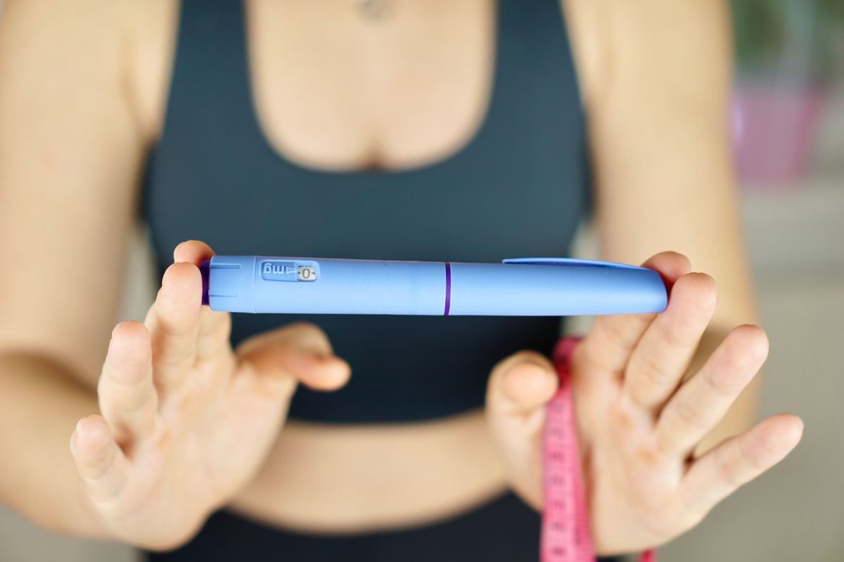 A girl in sportswear is holding an Ozempic insulin pen and a tape measure to measure her waist.
