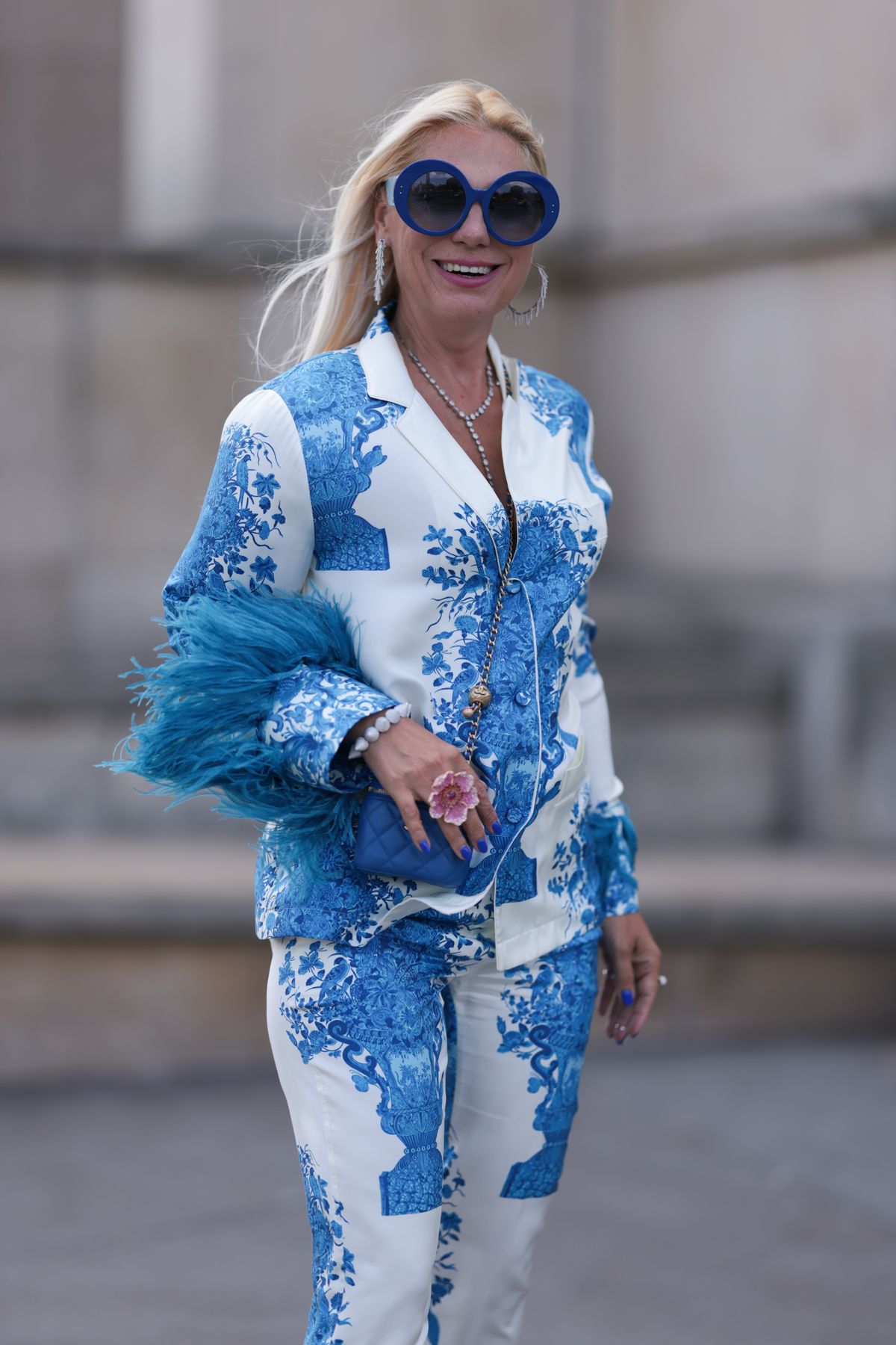 PARIS, FRANCE - JULY 03: Corina Mihaila Larpin seen outside Georges Hobeika show wearing blue round Paco Rabanne sunnies, Stefere diamond necklace and earrings, full Valentino suit in white with blue patterns and blue feathers, little blue Chanel leather handbag and pink plateau Amina Muaddi heels during the Haute Couture Fall/Winter 2023/2024 as part of  Paris Fashion Week on July 03, 2023 in Paris, France. (Photo by Jeremy Moeller/Getty Images)