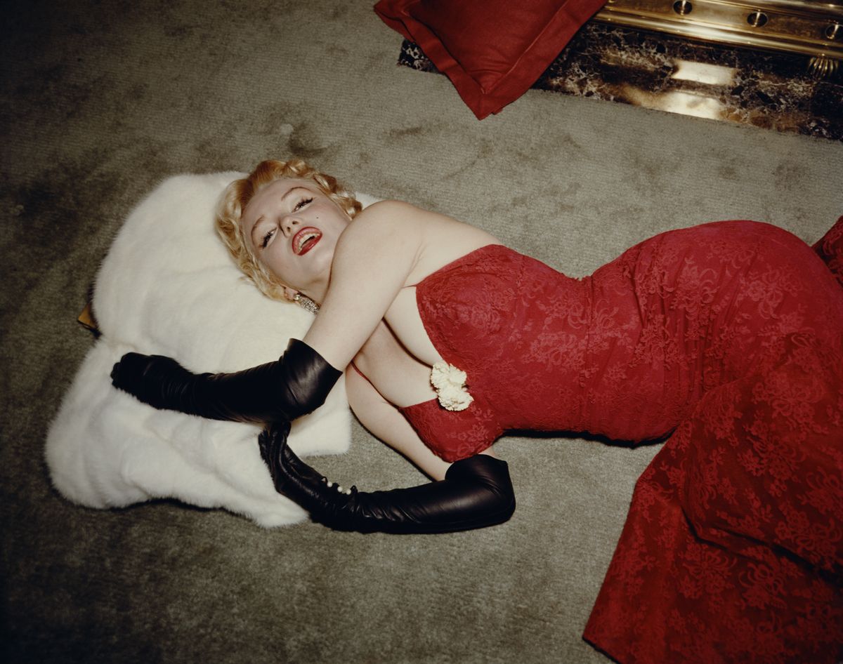 1955:  EXCLUSIVE American actor Marilyn Monroe (1926  - 1962), wearing a red brocade evening gown and long black gloves, lying on a carpet and using a white fur stole as a pillow.  (Photo by Gene Lester/Getty Images)