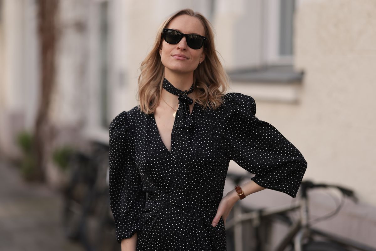 MUNICH, GERMANY - MARCH 22: Marlies Pia Pfeifhofer seen wearing Ray-Ban black Wayfarer sunglasses, gold necklace and silverearrings, Adoore black with white dotty print pattern v-neck midi long dress, matching Adoore black with white dotty print pattern small scarf and Cartier brown leather / gold watch, on March 22, 2024 in Munich, Germany. (Photo by Jeremy Moeller/Getty Images)