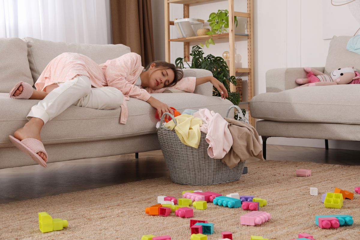 Tired young mother sleeping on sofa in messy living room