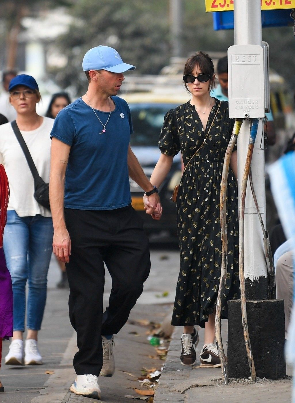 Bandra, INDIA  - *PREMIUM-EXCLUSIVE*  - Dakota Johnson and Chris Martin were spotted taking a leisurely stroll through Mumbai’s iconic Hanging Gardens, blending seamlessly into the lively surroundings. Walking hand-in-hand through a field of unknowing locals, the couple soaked in the vibrant atmosphere, even pausing to observe local 'Mumbaikers' passionately playing cricket nearby. Chris kept a firm hold on Dakota’s hand, notably free of any rings, as they navigated the bustling area. Dakota looked effortlessly chic in a DÔEN Haleigh Dress with a charming Buttercup Bouquet print, retailing for $400, paired with classic Nike Cortez sneakers and a vintage Céline bag. The duo appeared relaxed and in sync, savouring their time in the heart of the city

BACKGRID USA 21 JANUARY 2025,Image: 956134471, License: Rights-managed, Restrictions: , Model Release: no, Pictured: Chris Martin, Dakota Johnson