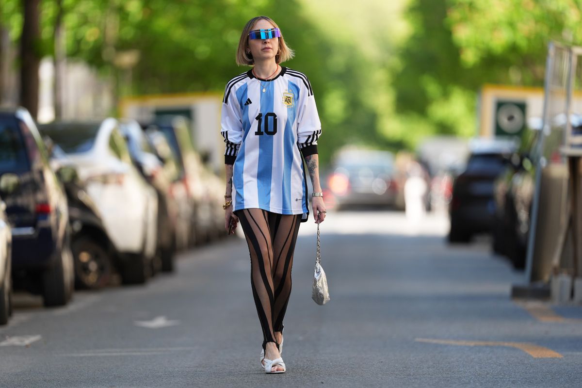 PARIS, FRANCE - APRIL 13: Emy Venturini wears sunglasses from Pierre Cardin, a Cartier watch, a blue and white striped Argentina soccer t-shirt from Adidas with printed "10" on the front and "Messi" on the back, black mesh striped stirrup leggings from Mugler, a silver bag from Rabanne, kitten heels white leather Balenciaga shoes, during a street style fashion photo session, on April 13, 2024 in Paris, France. (Photo by Edward Berthelot/Getty Images)