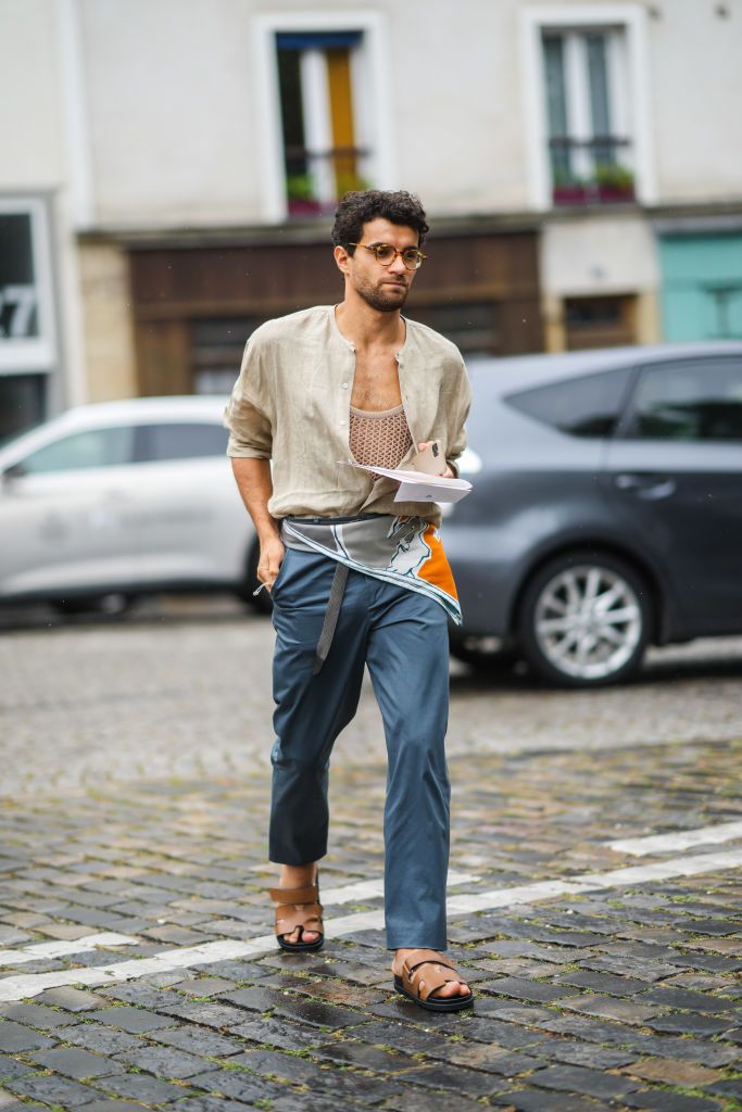PARIS, FRANCE - JUNE 26: A guest wears glasses, a beige mesh t-shirt, a beige linen shirt, a gray orange and white scarf as a belt, blue suit pants, brown shiny leather sandals from Hermes, outside Hermes, during Paris Fashion Week - Menswear Spring/Summer 2022, on June 26, 2021 in Paris, France. (Photo by Edward Berthelot/Getty Images)