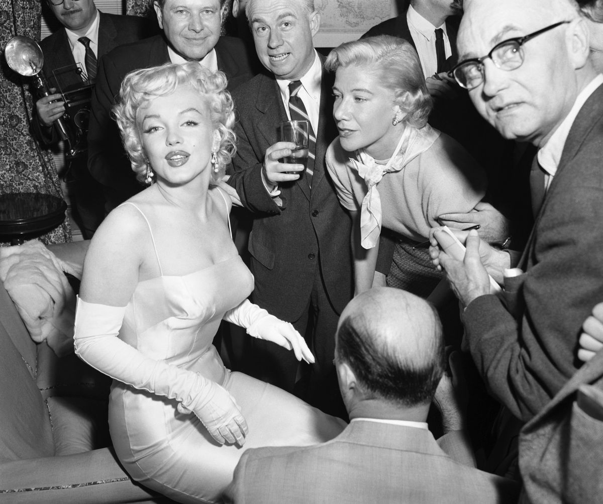 Actress Marilyn Monroe (L) is surrounded by photographers and journalists as she is interviewed by Phyllis Battelle (R), who writes in the International News Service column Assignment: America. Miss Monroe unveiled her new look for friends and the press at the cocktail party.