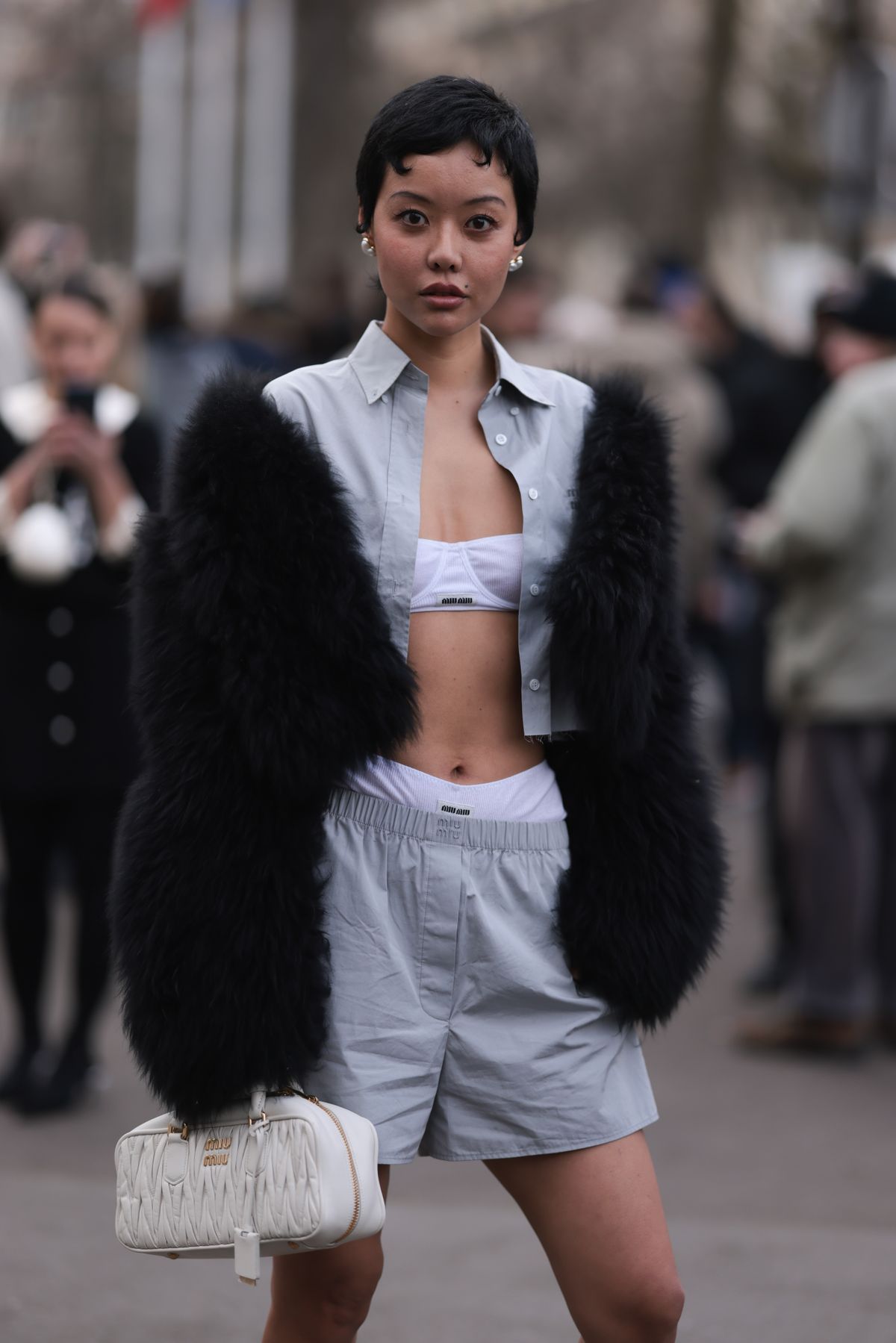 PARIS, FRANCE - MARCH 05: A guest seen wearing Miu Miu white underwear, Miu Miu grey shirt, matching Miu Miu grey shorts, a fur jacket and Miu Miu white handbag outside Miu Miu Show during the Womenswear Fall/Winter 2024/2025 as part of  Paris Fashion Week on March 05, 2024 in Paris, France. (Photo by Jeremy Moeller/Getty Images)