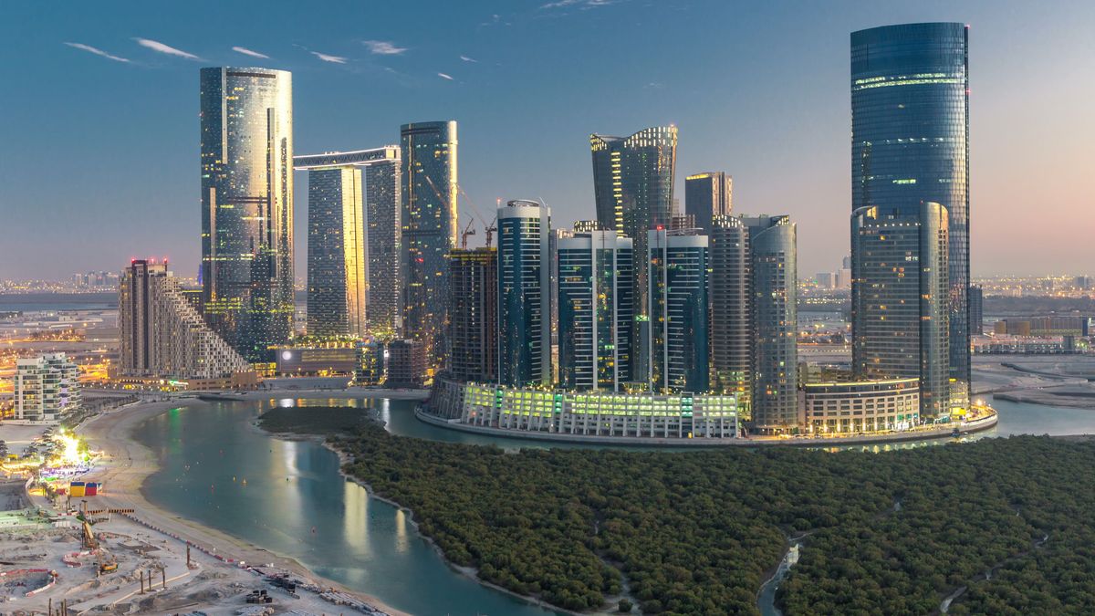 Skyscrapers on Al Reem Island in Abu Dhabi day to night transition timelapse after sunset from above. Aerial cityscape from Al Reem Island with illuminated buildings