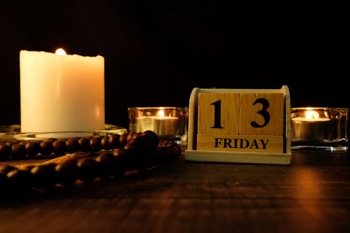 péntek 13 13 FRIDAY word written on wood block with burning candles and prayer wood beads.Mystic and darkness background.