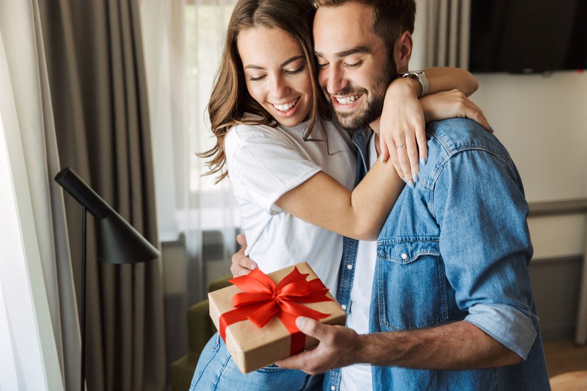 Beautiful young couple in love at home, celebrating with a gift box exchange, hugging