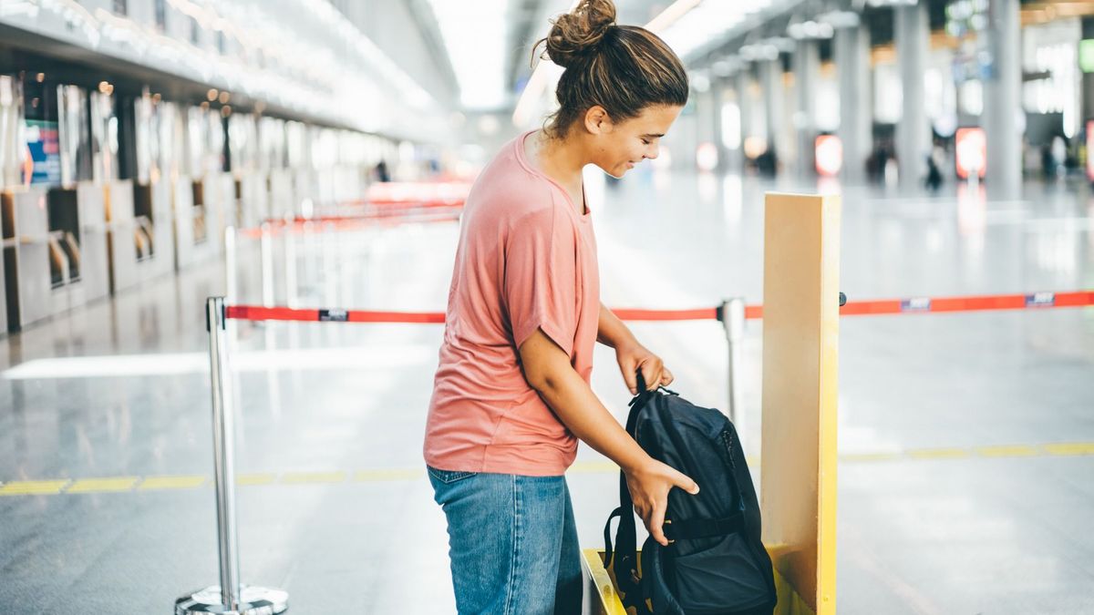 Woman checking size of her carry-on luggage at airport.