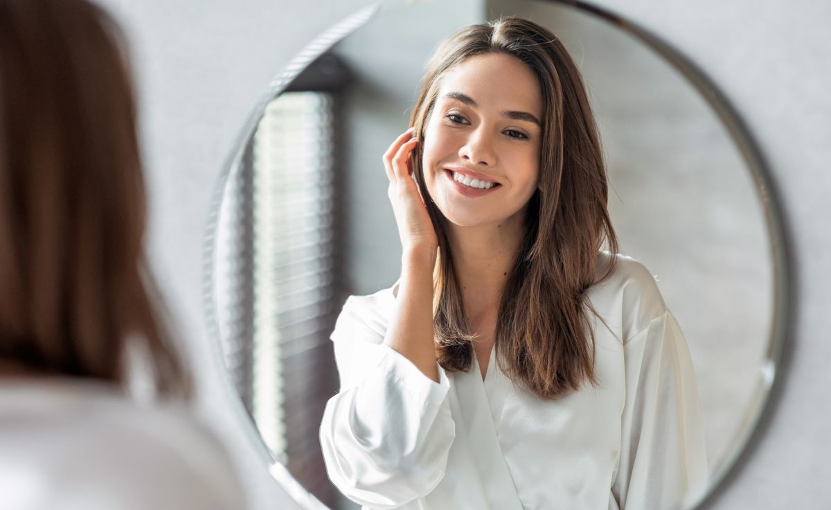 Beauty Concept. Portrait Of Attractive Happy Woman Looking At Mirror In Bathroom, Beautiful Millennial Lady Wearing White Silk Robe Smiling To Reflection, Enjoying Her Appearance, Selective Focus
